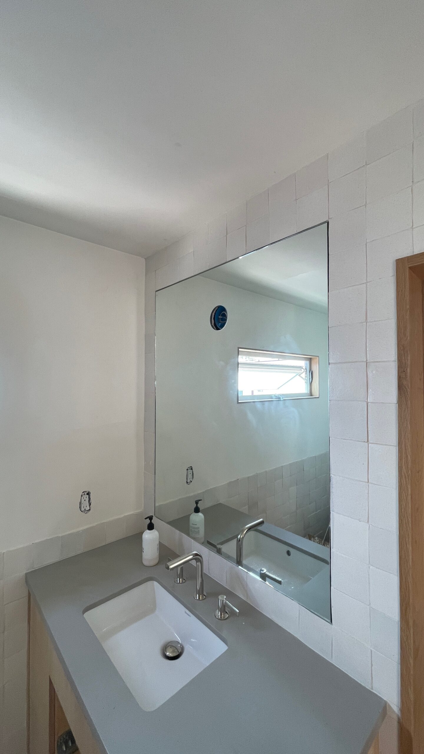 Custom-cut bathroom vanity mirror with frameless edge above sink and tiled backsplash