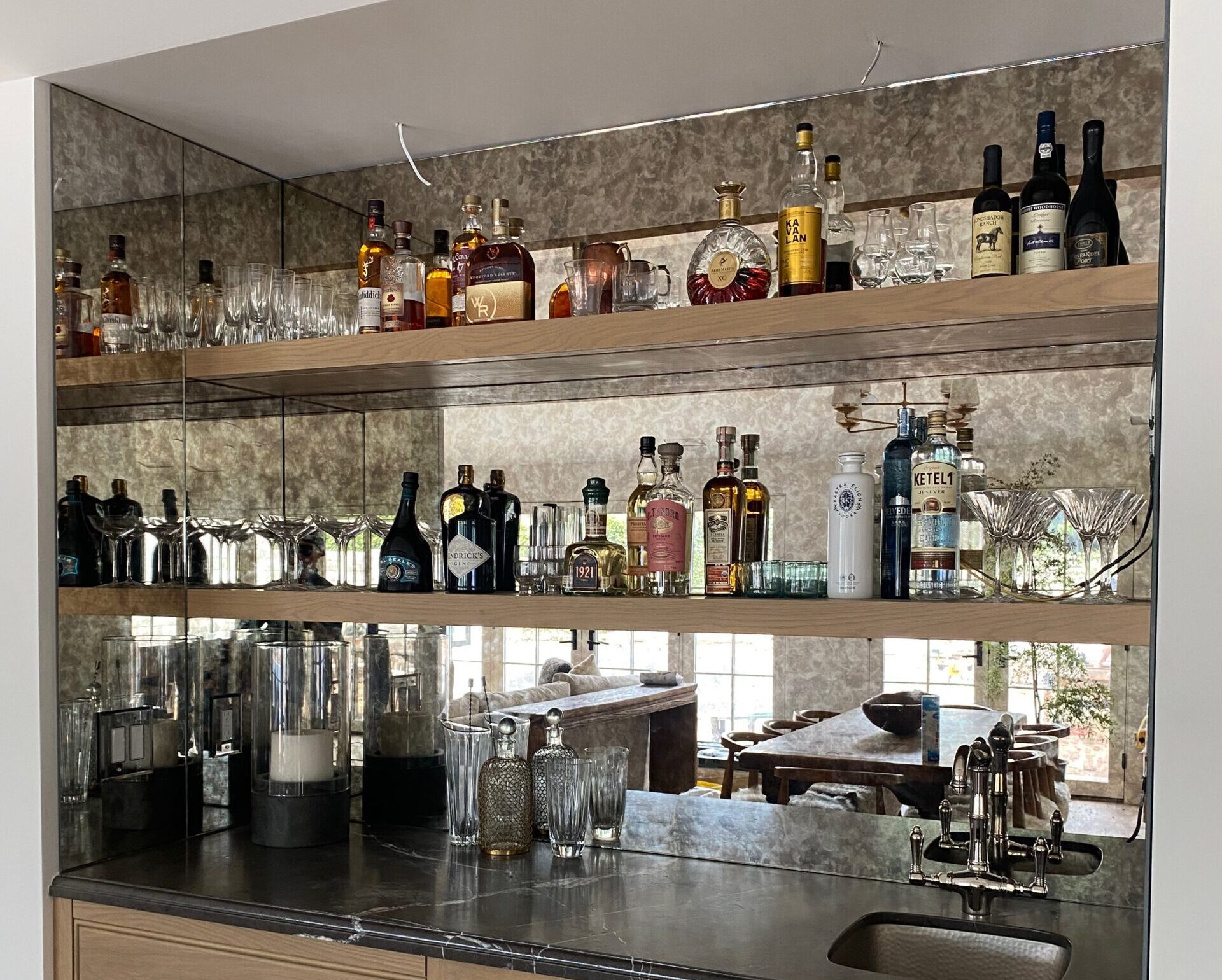 Custom mirror backsplash installed in home bar with glass shelving and wood cabinetry